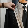 A tailor uses a tape measure on a suit jacket displayed on a mannequin, showcasing the craft of tailoring.