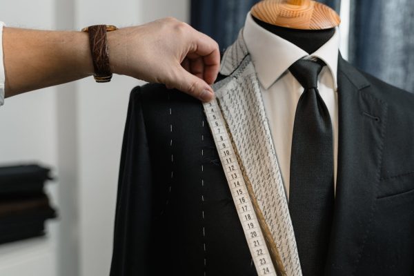 A tailor uses a tape measure on a suit jacket displayed on a mannequin, showcasing the craft of tailoring.